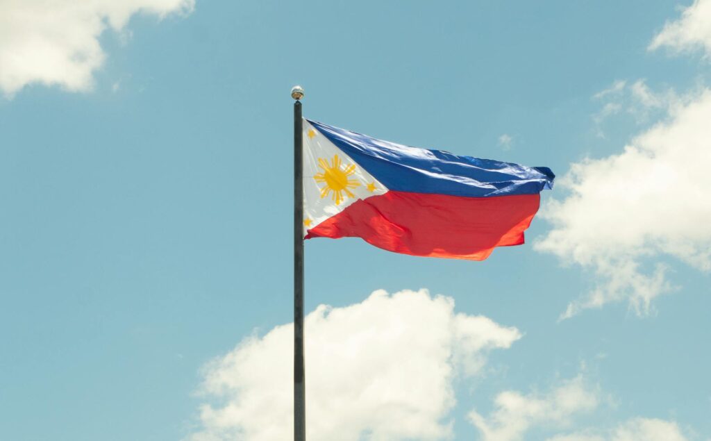 pexels-photo-32351333-32351333 The national flag of the Philippines waving proudly in a clear blue sky with clouds.
